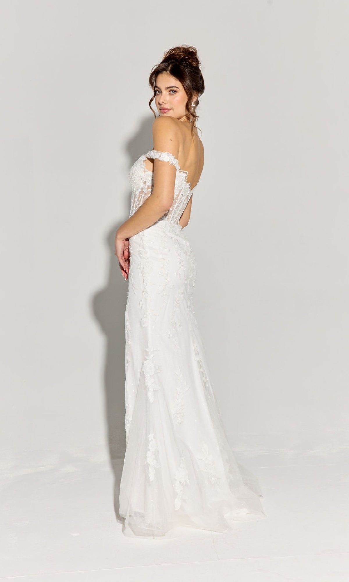 A woman wearing the Eureka EK181 Off-Shoulder Long Lace Prom Dress with floral lace embroidery stands against a plain light background, looking over her shoulder in an elegant pose.
